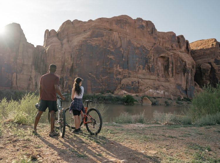 Man and woman with bikes standing next to a river in the Moab desert