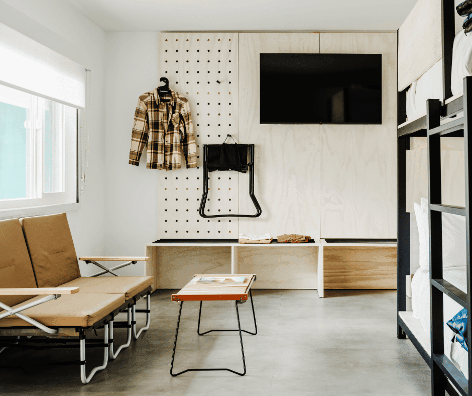 A hotel room with bunk beds, a couch and coffee table, and a bench along the wall with a TV hanging above