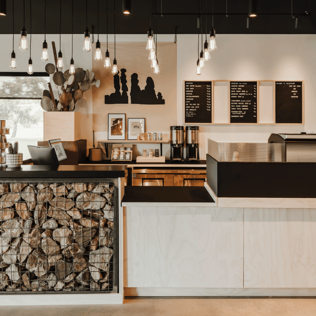 A cafe counter with a menu board behind it. Part of the counter is made of rocks, and the other part is white with a black top.