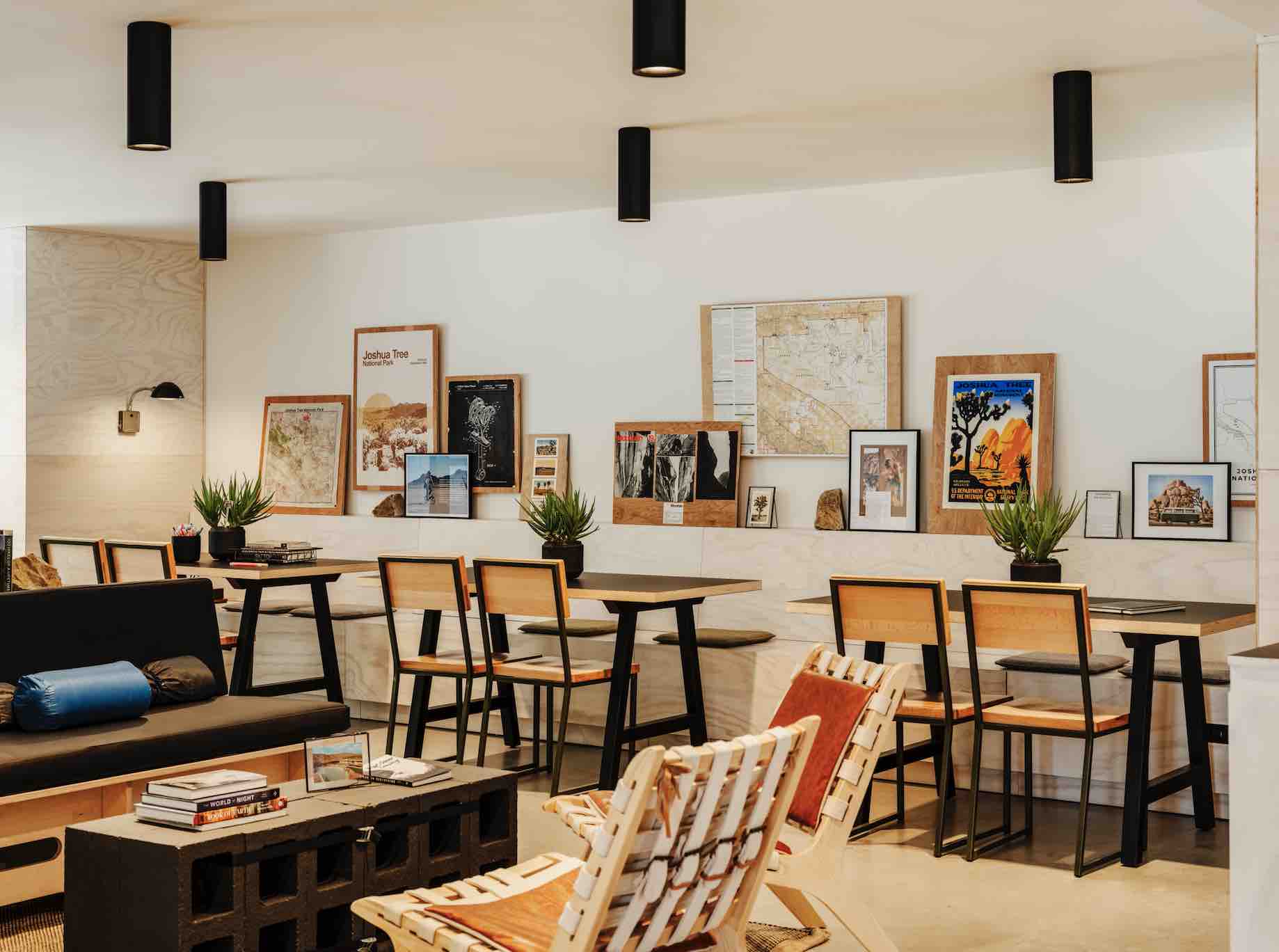 A white and wood cafe with multiple sets of tables and chairs, and art/posters along a sill on the wall