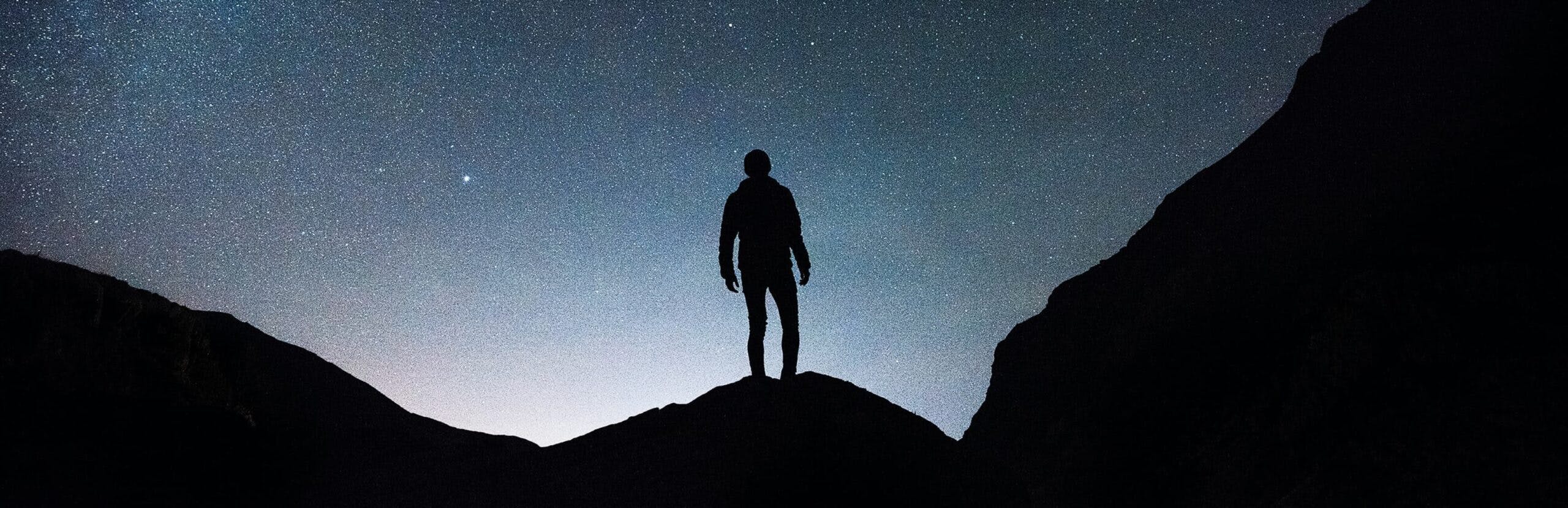 silhouette of a man standing on top of a rock cliff stargazing sky dense with stars